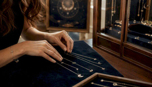 Hands arranging zodiac-themed gold necklaces